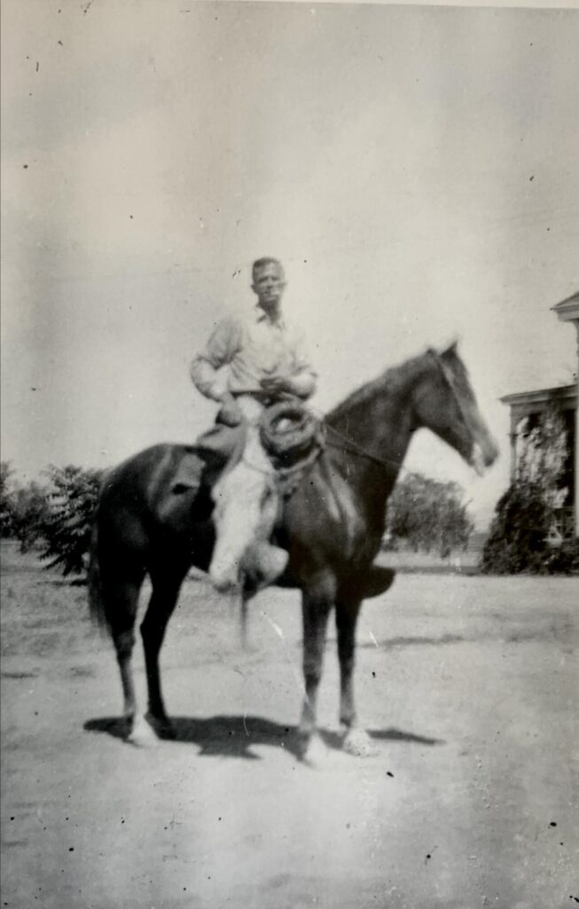 Black and white 1920s photo of a grown Joseph Connolly (2d Generation) sitting on horse on the ranch, smoking a cigarette.