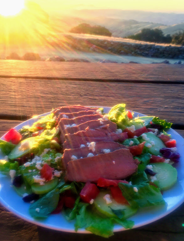 Salad with Connolly Ranch beef sliced on top, on table outside with setting sun in the background.