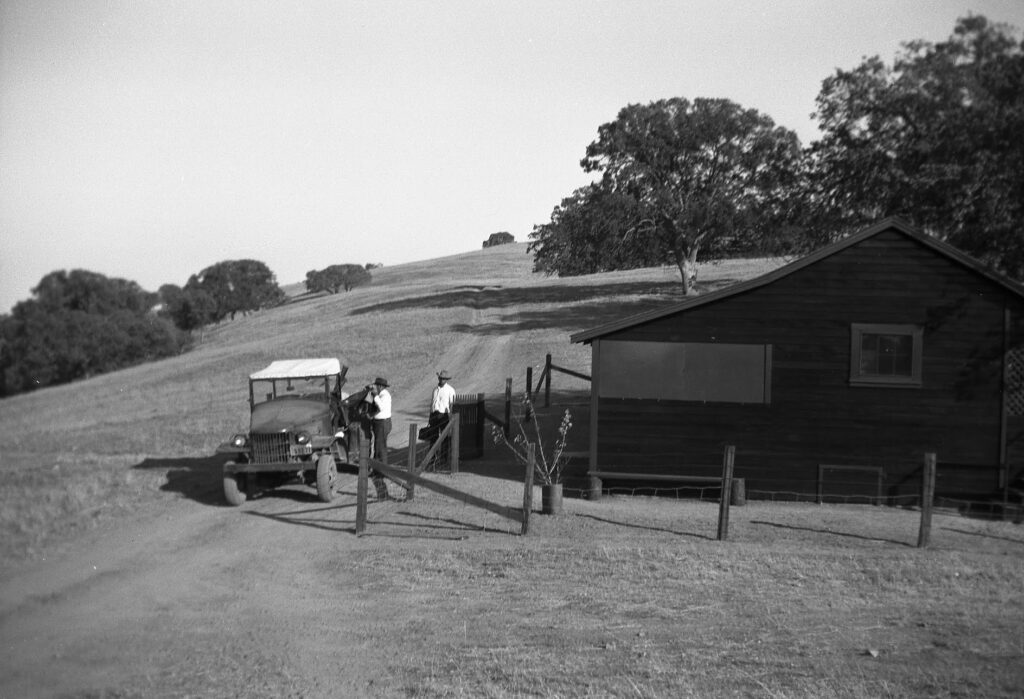 Black and white 1950s historic photo of sheepherder’s cabin and vehicle on the ranch.